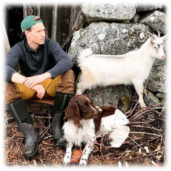 En bonde sitter på bakken sammen med en hund og ei geit. Bonden ser tankefullt ut i lufta. - Klikk for stort bilde